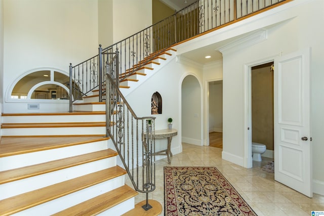 staircase with crown molding, a towering ceiling, and tile patterned floors