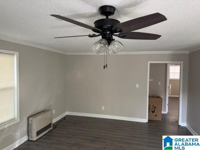 spare room with heating unit, dark wood-type flooring, ornamental molding, and ceiling fan