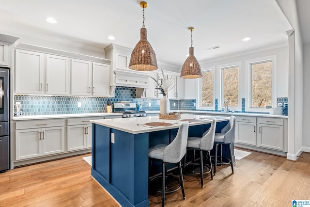 kitchen with decorative light fixtures, a center island, ornamental molding, stainless steel stove, and white cabinets