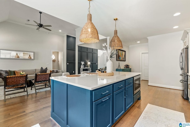 kitchen featuring blue cabinetry, wood-type flooring, an island with sink, pendant lighting, and stainless steel appliances