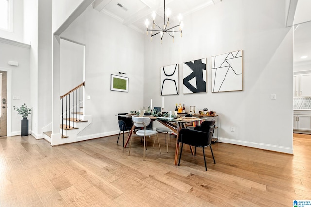 dining room featuring beamed ceiling, an inviting chandelier, light hardwood / wood-style flooring, and a high ceiling