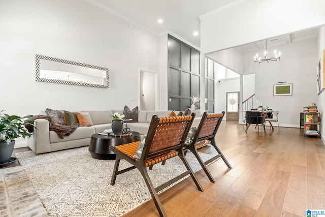 living room with crown molding, a towering ceiling, a notable chandelier, and light hardwood / wood-style floors