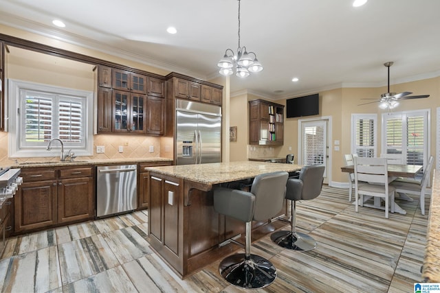 kitchen featuring appliances with stainless steel finishes, sink, a kitchen bar, a center island, and light stone counters