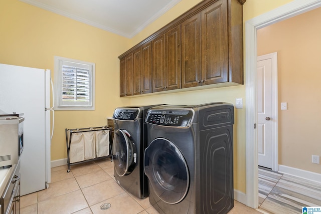 clothes washing area featuring crown molding, cabinets, washing machine and dryer, and light tile patterned floors