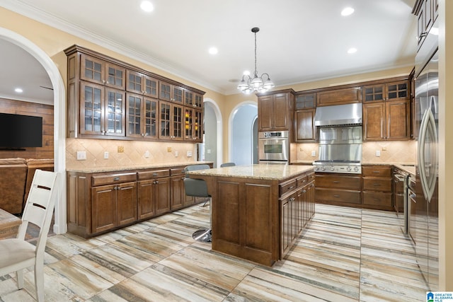 kitchen featuring wall chimney exhaust hood, decorative light fixtures, a center island, ornamental molding, and stainless steel appliances