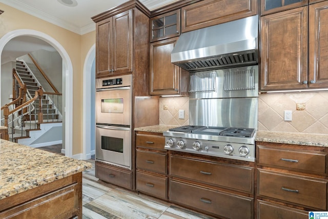 kitchen featuring stainless steel appliances, crown molding, light stone countertops, and exhaust hood