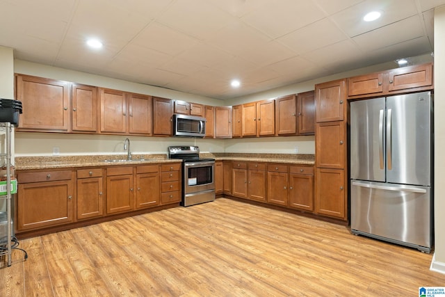 kitchen with stainless steel appliances, light stone countertops, sink, and light wood-type flooring