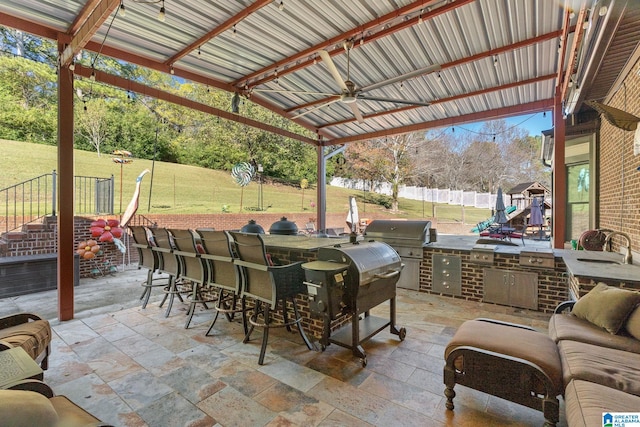 view of patio featuring ceiling fan, area for grilling, a playground, and a wet bar