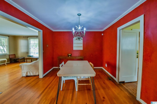 dining space with hardwood / wood-style flooring, ornamental molding, and an inviting chandelier