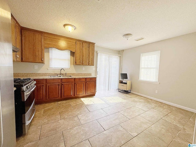 kitchen featuring gas range, light tile patterned flooring, sink, and a textured ceiling