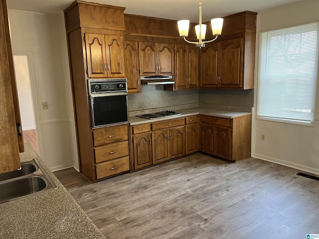 kitchen featuring sink, decorative light fixtures, light wood-type flooring, black oven, and backsplash