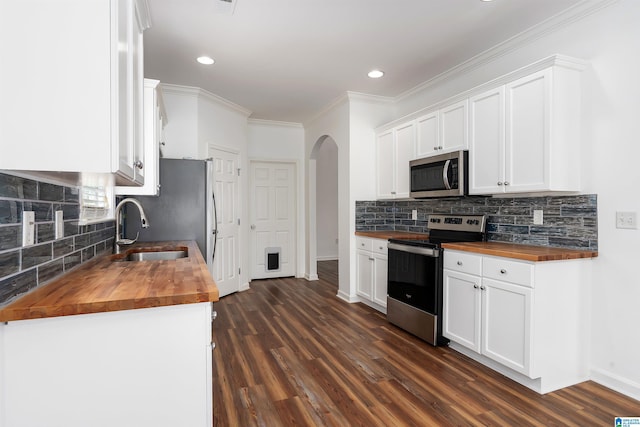 kitchen featuring appliances with stainless steel finishes, butcher block countertops, sink, backsplash, and white cabinets