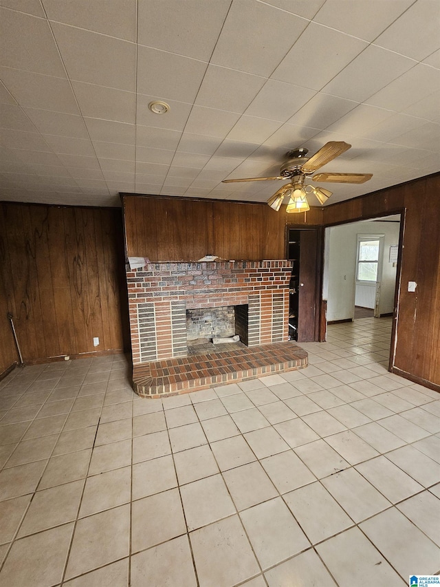 unfurnished living room with light tile patterned flooring, a fireplace, and wood walls