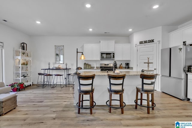 kitchen featuring a kitchen island with sink, light stone countertops, a kitchen breakfast bar, and appliances with stainless steel finishes