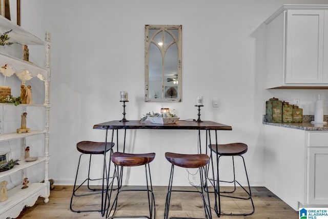 bar featuring light hardwood / wood-style flooring, dark stone counters, and white cabinets