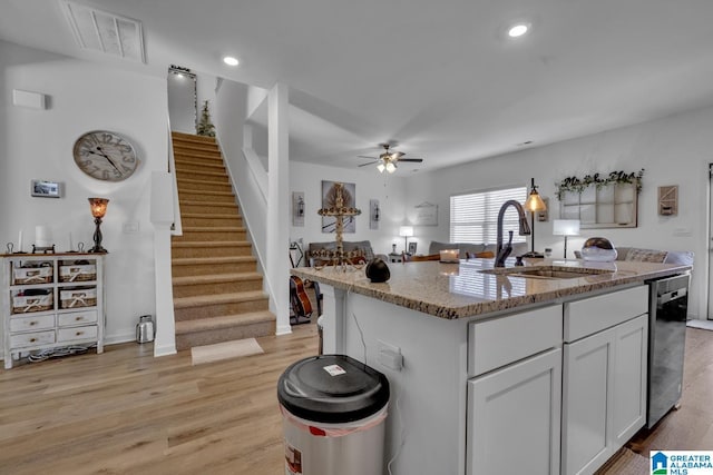 kitchen with dishwasher, sink, white cabinets, light stone counters, and a center island with sink