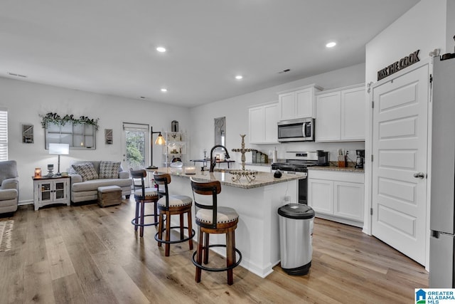 kitchen featuring light stone counters, light wood-type flooring, stainless steel appliances, a kitchen island with sink, and white cabinets