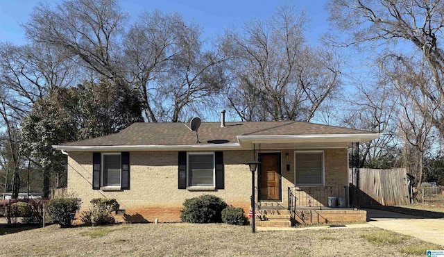 view of front facade with fence, a shingled roof, and brick siding