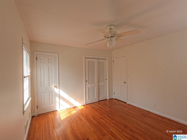 unfurnished bedroom with two closets, hardwood / wood-style floors, and ceiling fan