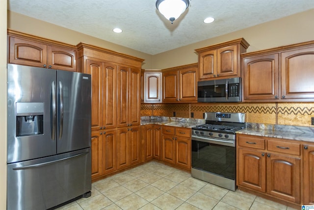 kitchen featuring backsplash, light tile patterned floors, stainless steel appliances, and dark stone counters