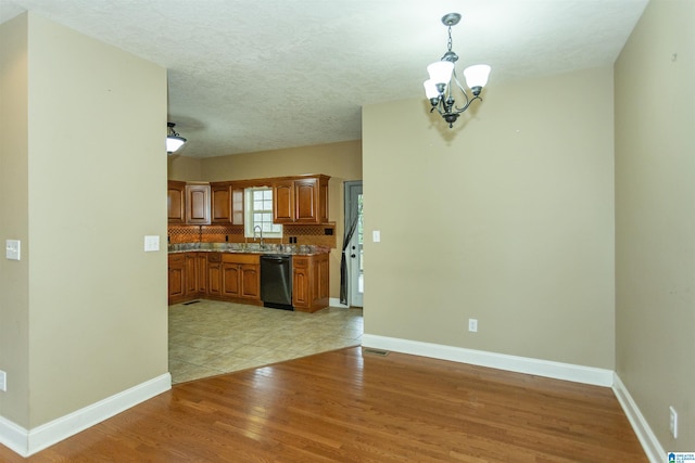 kitchen featuring pendant lighting, tasteful backsplash, dishwasher, sink, and light hardwood / wood-style floors