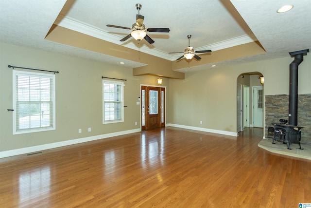 unfurnished living room with crown molding, a tray ceiling, and a wood stove