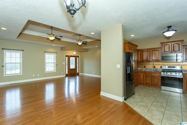 kitchen with tasteful backsplash, light wood-type flooring, ornamental molding, a tray ceiling, and stainless steel appliances