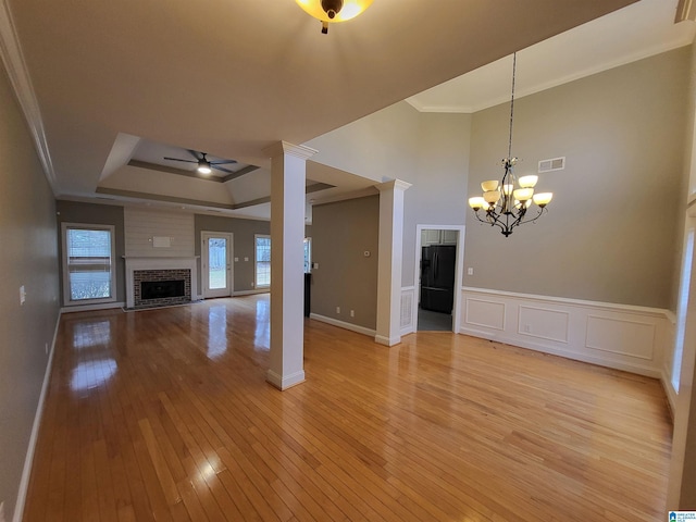 unfurnished living room with ornate columns, a raised ceiling, crown molding, a brick fireplace, and light hardwood / wood-style flooring