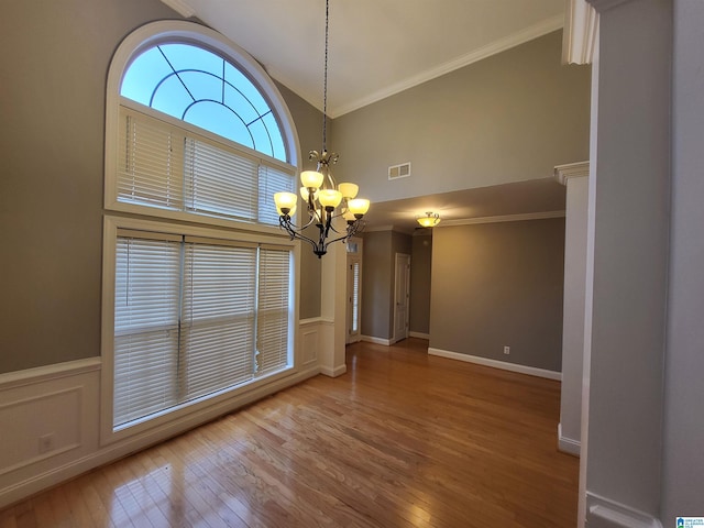 unfurnished dining area featuring an inviting chandelier, high vaulted ceiling, hardwood / wood-style flooring, and ornamental molding