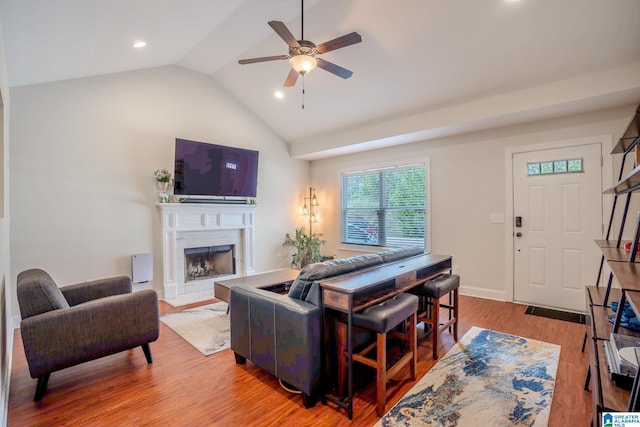 living room with ceiling fan, wood-type flooring, a premium fireplace, and vaulted ceiling