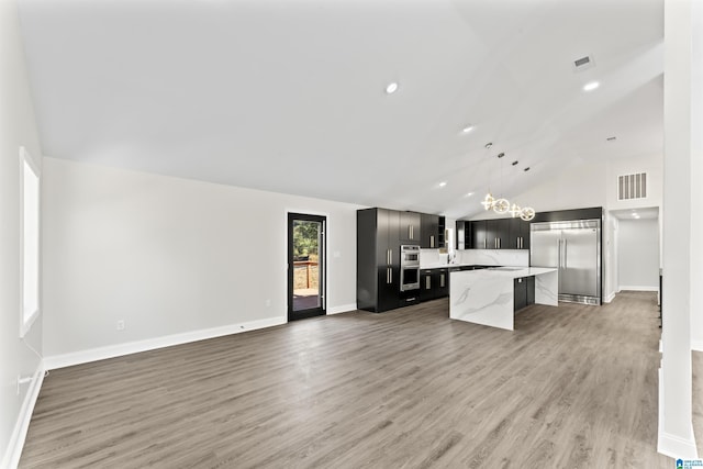 kitchen with a kitchen island, pendant lighting, lofted ceiling, stainless steel appliances, and light stone countertops