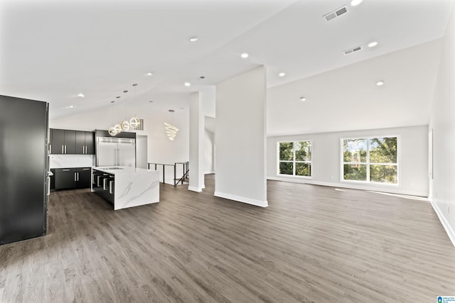 kitchen with pendant lighting, built in refrigerator, a center island, light stone countertops, and dark hardwood / wood-style flooring