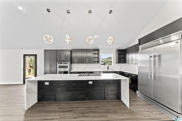 kitchen with stainless steel appliances, light stone countertops, decorative backsplash, a kitchen island, and decorative light fixtures