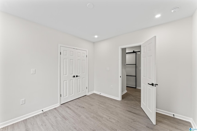 unfurnished bedroom with a closet, a barn door, and light hardwood / wood-style flooring