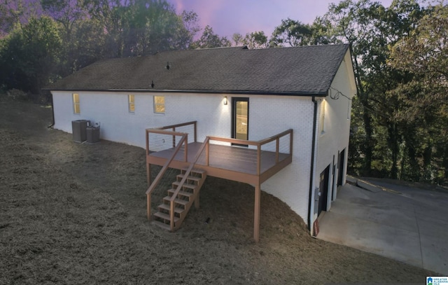 back house at dusk with a garage, central AC unit, and a deck