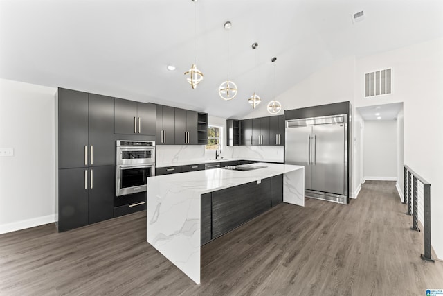 kitchen with appliances with stainless steel finishes, dark hardwood / wood-style flooring, hanging light fixtures, a center island, and light stone countertops