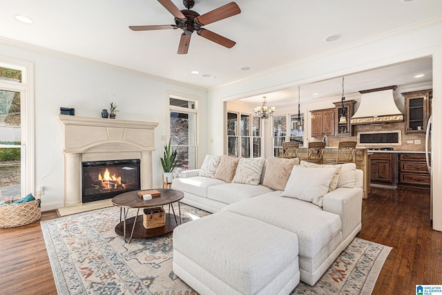 living room featuring crown molding, dark wood-type flooring, and ceiling fan with notable chandelier