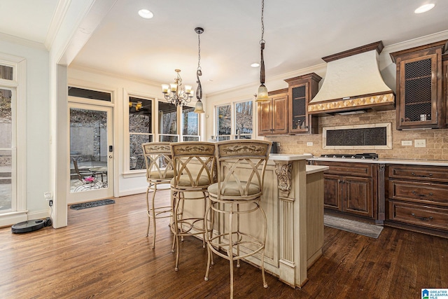 kitchen featuring premium range hood, backsplash, a center island, stainless steel gas cooktop, and dark wood-type flooring