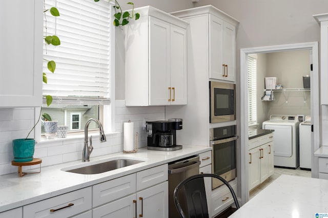 kitchen with sink, appliances with stainless steel finishes, white cabinetry, tasteful backsplash, and separate washer and dryer