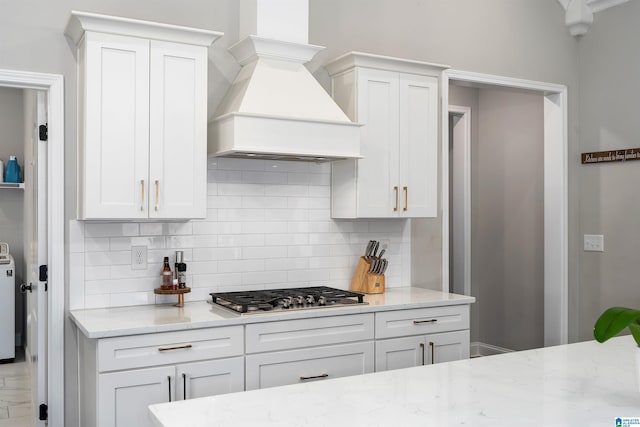 kitchen with stainless steel gas stovetop, white cabinets, decorative backsplash, custom exhaust hood, and light stone countertops