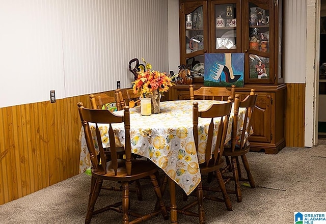 carpeted dining area featuring wooden walls