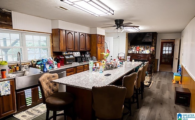 kitchen with an island with sink, a breakfast bar area, ceiling fan, and dark hardwood / wood-style flooring