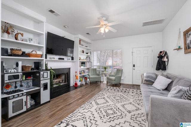 living room with dark hardwood / wood-style flooring, built in features, a tile fireplace, and ceiling fan