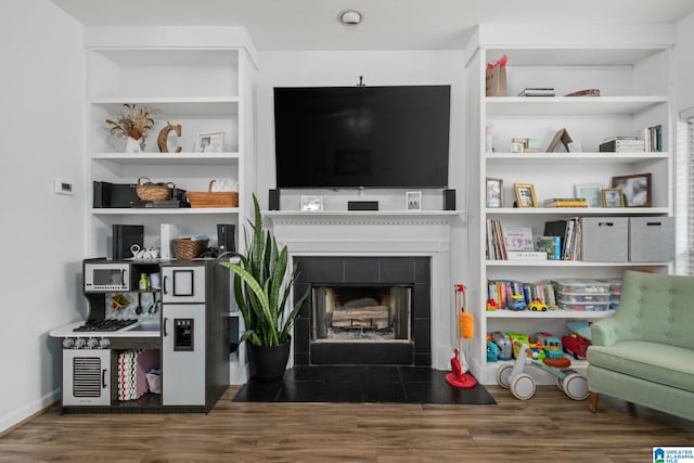 living room with built in shelves, dark wood-type flooring, and a tile fireplace