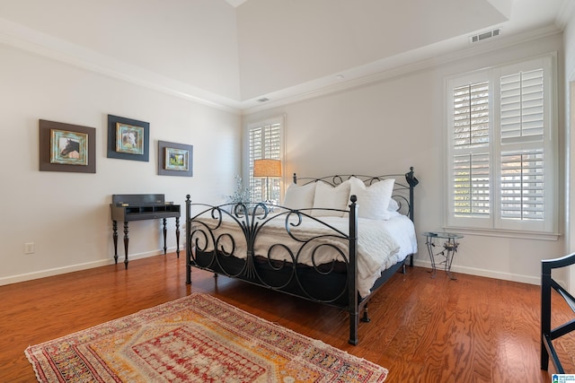 bedroom featuring wood-type flooring, ornamental molding, and a high ceiling