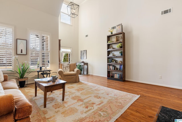 living room with hardwood / wood-style flooring, a towering ceiling, and an inviting chandelier