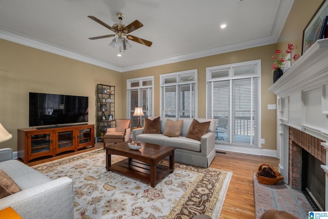 living room with ceiling fan, ornamental molding, a fireplace, and light wood-type flooring