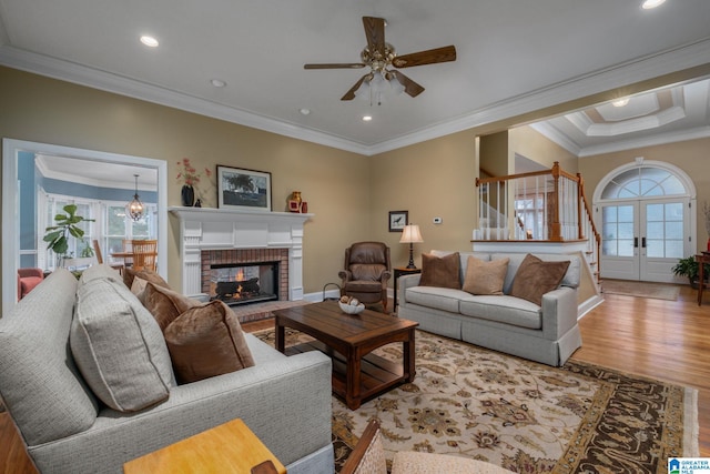 living room featuring crown molding, ceiling fan, hardwood / wood-style floors, a brick fireplace, and french doors