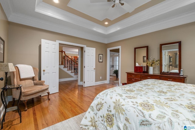 bedroom with ceiling fan, ornamental molding, a tray ceiling, and light wood-type flooring