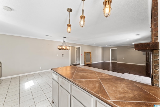 kitchen with pendant lighting, light tile patterned floors, crown molding, white cabinetry, and a textured ceiling